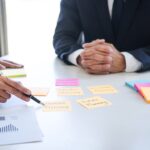 Deux hommes en costumes discutent de planification financière, avec des notes et des graphiques