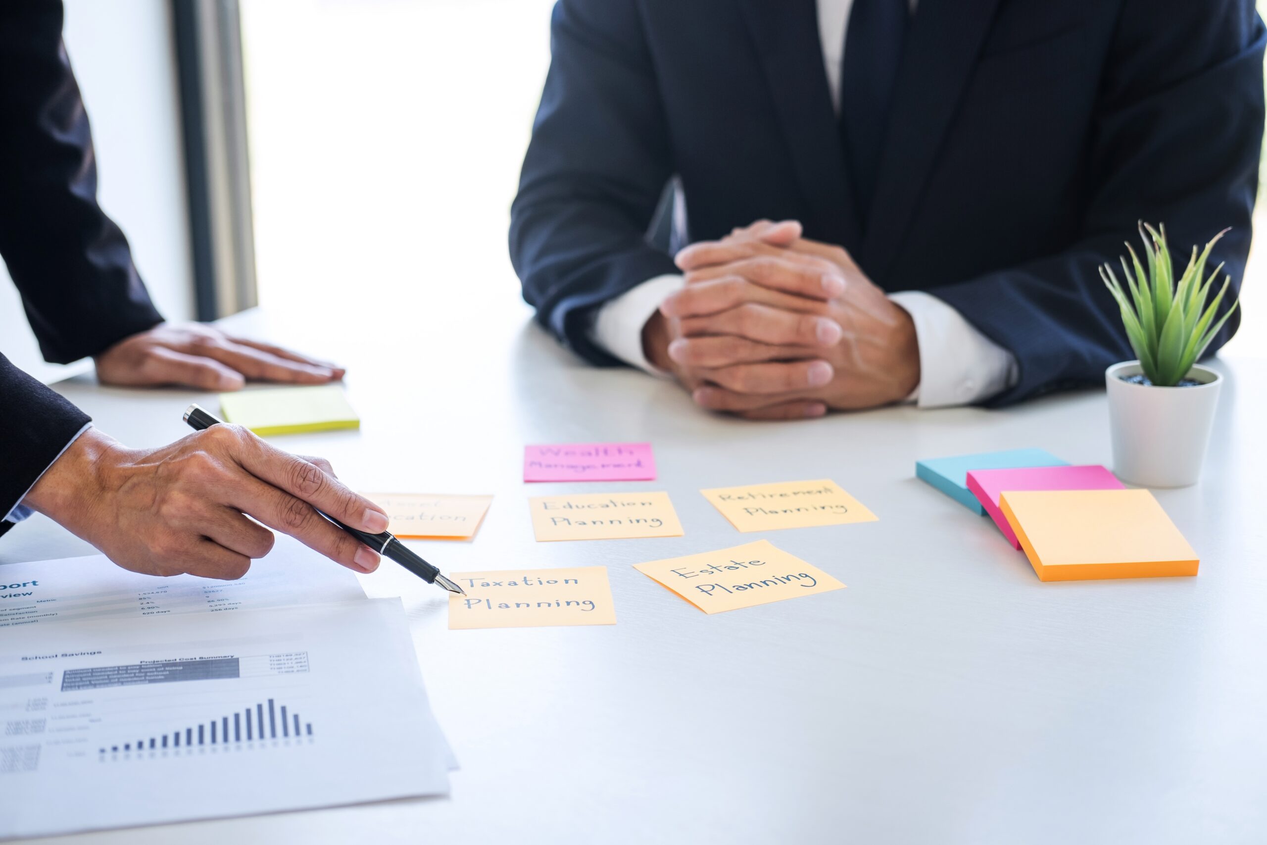 Deux hommes en costumes discutent de planification financière, avec des notes et des graphiques