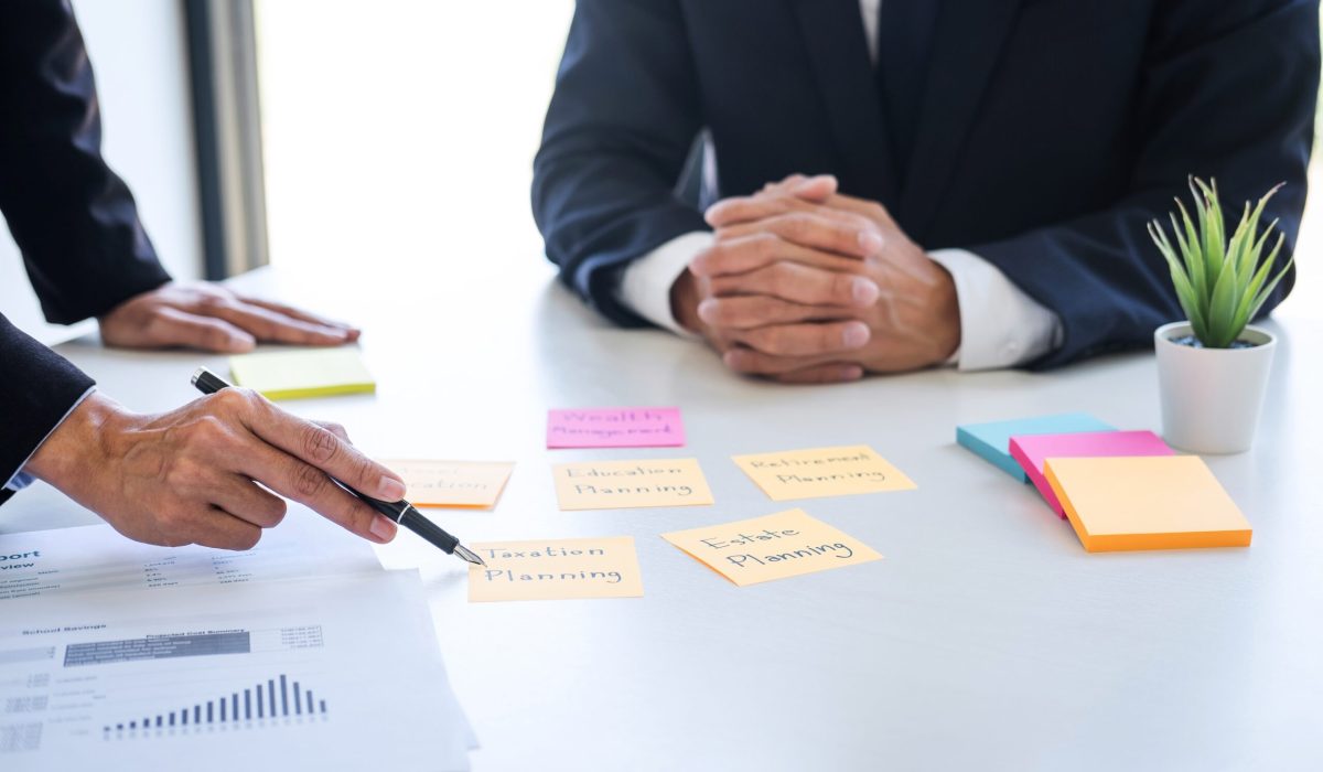 Deux hommes en costumes discutent de planification financière, avec des notes et des graphiques