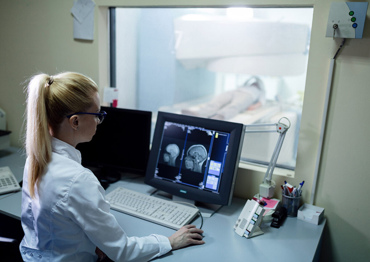 Radiologist analyzing brain MRI scan results of a patient on computer monitor in control room.