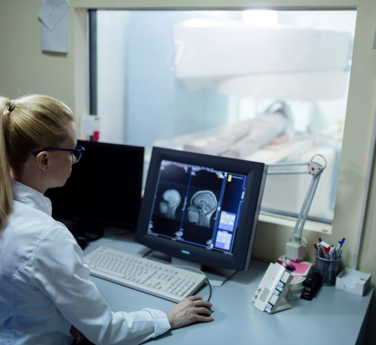 Radiologist analyzing brain MRI scan results of a patient on computer monitor in control room.